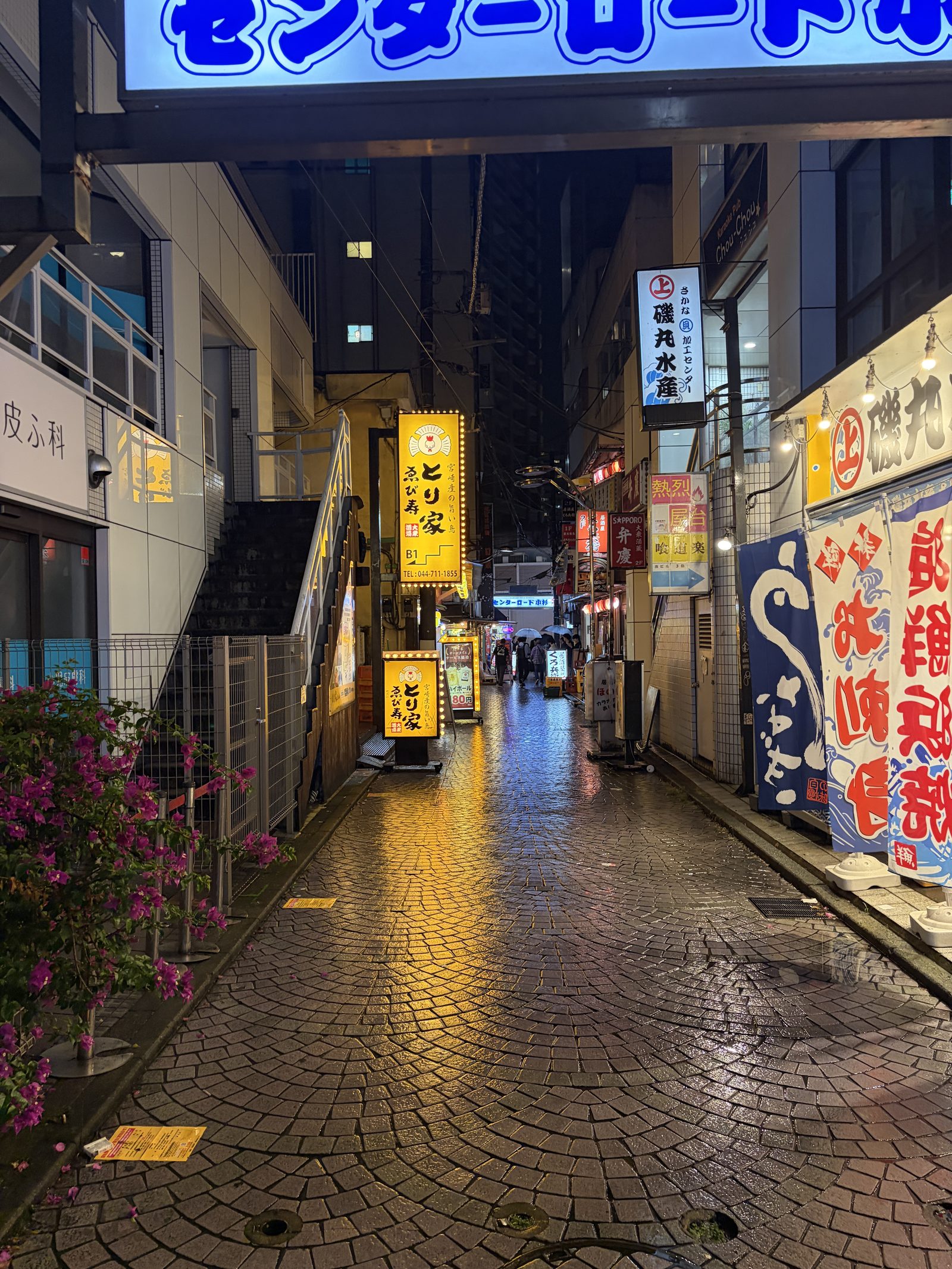 A rain-wet cobblestone alley at night, lined with glowing Japanese restaurant signs and banners.